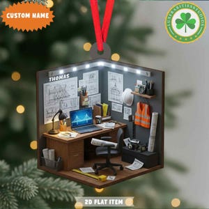 May include: A 3D-style ornament depicting an engineer's office, complete with a desk, laptop, blueprints, and safety vest. The ornament has a red ribbon for hanging and features the text "CUSTOM NAME" and "2D FLAT ITEM". The office is lit with small lights.