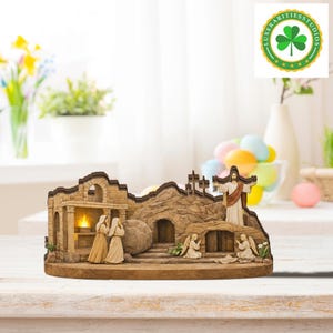 Può includere: Una scultura in legno dettagliata a tema pasquale che raffigura la risurrezione di Gesù. La scultura presenta figure di Gesù, angeli e donne vicino a una tomba, con una pietra rotolata via. La tavolozza dei colori include tonalità beige, marrone e oro.