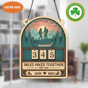 Könnte beinhalten: Holzschild zum Thema Wandern mit Berg- und Waldmotiv. Enthält den Text "MILES HIKED TOGETHER THIS YEAR" und die Namen "JOHN" und "EMILY". Enthält die Zahlen "345" und einen Abschnitt "CUSTOM NAME".