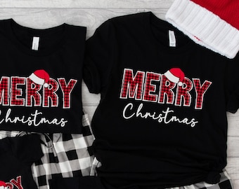 May include: Black Christmas shirts with "MERRY Christmas" in red plaid lettering and a Santa hat graphic. The shirts are paired with black and white plaid pajama pants. Red and white Santa hats are also visible.