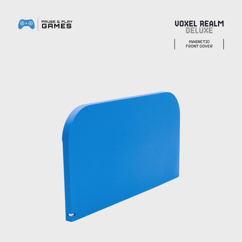 May include: A bright blue magnetic front cover for a gaming console. The cover has rounded corners and a small white detail at the bottom. The text "VOXEL REALM DELUXE" is printed on the top right.