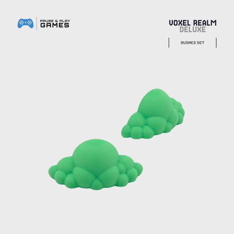 May include: Two green, cloud-shaped objects, possibly miniature terrain elements, are displayed against a light background. The objects are part of the "Voxel Realm Deluxe" series, as indicated by the text in the upper right corner. The logo for "Pause & Play Games" is in the upper left.