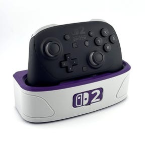 May include: A black Nintendo Switch Pro Controller in a white and purple charging dock. The controller has buttons labeled X, Y, A, and B. The dock has the Nintendo Switch logo.