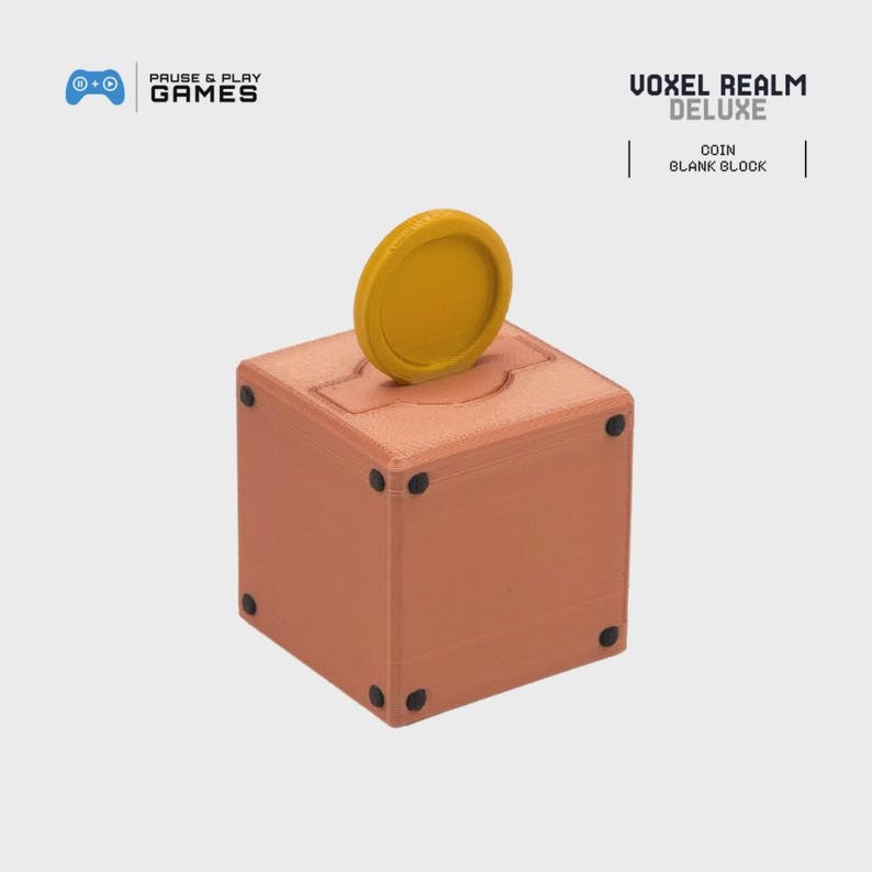 May include: A brown, cube-shaped coin bank with a gold coin inserted into the top slot. The bank has black dots on each corner. The text "VOXEL REALM DELUXE" and "COIN BLANK BLOCK" are printed on the image.