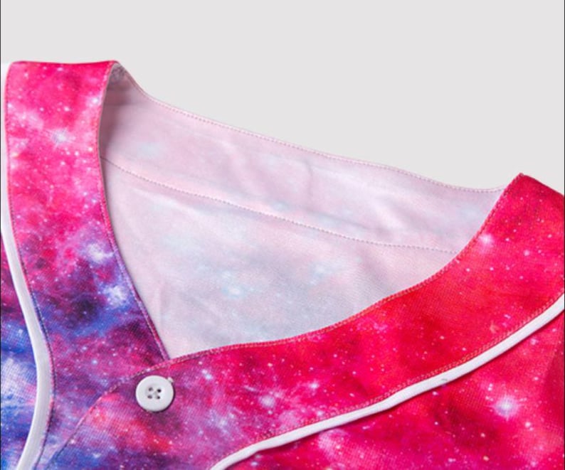 May include: A baseball jersey with a vibrant galaxy print in shades of pink, purple, and blue. The jersey features a white collar and button closure. The design resembles a nebula, with white accents outlining the edges.