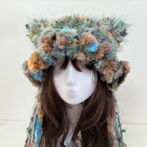 May include: A distinctive, handmade hat with a textured design. The hat combines blue, brown, and orange yarn, creating a fluffy, eye-catching appearance. The hat has a brim and ear-like accents, adding to its unique style and appeal.