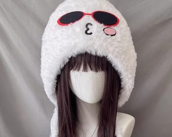 Puede incluir: Sombrero blanco y difuso con un diseño de cara de dibujos animados. El sombrero presenta gafas de sol negras con montura roja, un número 3 negro y una mejilla rosa. El sombrero está diseñado para ser usado en la cabeza.