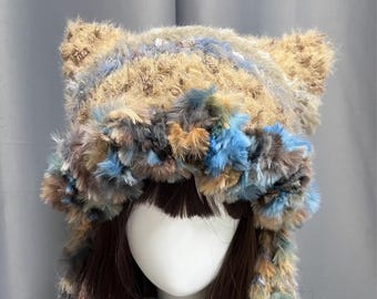 May include: A fluffy, multi-colored hat with cat ears. The hat features a mix of brown, blue, and tan faux fur. The hat is designed to be worn on the head and has a soft, textured appearance. The hat is a unique accessory.