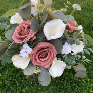 May include: A bouquet of blush pink roses, white calla lilies, and white baby's breath with eucalyptus greenery.