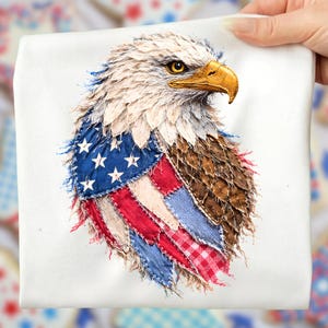 Pode incluir: Um tecido quadrado branco com uma aplicação de uma águia careca americana. A cabeça da águia é feita com tecido branco e castanho texturizado, um bico amarelo e um olho amarelo. O peito da águia apresenta um design de patchwork da bandeira americana.