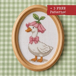 Può includere: Un ricamo a punto croce in una cornice ovale di legno raffigurante un'anatra bianca che indossa un cappello a fiore rosa e un papillon rosa. L'anatra ha becco e zampe arancioni. Il testo + 3 FREE Patterns è stampato nell'angolo in alto a destra.