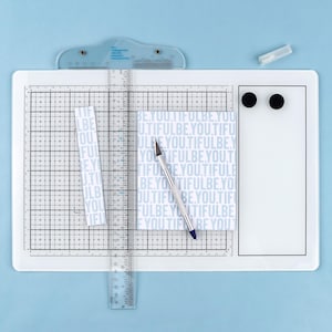May include: A white cutting mat with a grid pattern, ruler, and a craft knife. The mat has a light blue background and includes a small piece of paper with the text "BE YOU.TIFULBE.YOU".