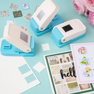 May include: Three blue and white stamp-shaped paper punches with a variety of colorful stamps and cut-out paper. The stamps feature floral and architectural designs. The background is a light blue surface.