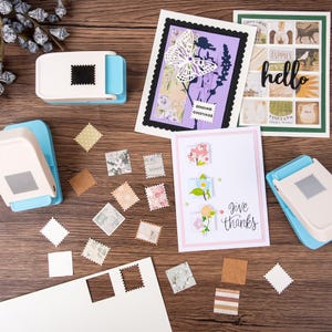 May include: A craft scene with handmade greeting cards and stamp-shaped paper cutouts. The cards feature floral designs, butterfly cutouts, and the words "hello" and "give thanks." Two blue and white stamp-shaped paper punches are also visible.