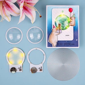 Könnte beinhalten: Eine Sammlung von Bastelmaterialien auf blauem Untergrund. Enthält transparente Kunststoffkuppeln, LED-Leuchtkreise, einen metallenen Stanzkreis und eine Grußkarte mit Bärenillustrationen, Geschenken und dem Text "BEARY SPECIAL Day".