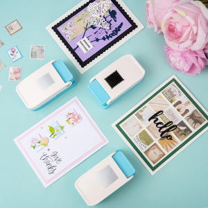 May include: A collection of handmade greeting cards and craft supplies. The cards feature floral and butterfly designs, with the words "hello" and "give thanks". Several white and blue stamp-shaped paper punches are also visible.