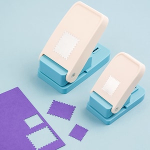 May include: Two stamp-shaped paper punches with a light blue base and off-white top. A purple sheet of paper with stamp-shaped cutouts and three purple stamps are also visible on a light blue background.