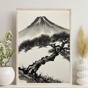 以下が含まれることがあります： 山と松の木を描いた、額入りの白黒インク画。 アートワークは明るい色の木製の棚に展示されており、白い花瓶と乾燥した草が入った白い花瓶が置かれています。