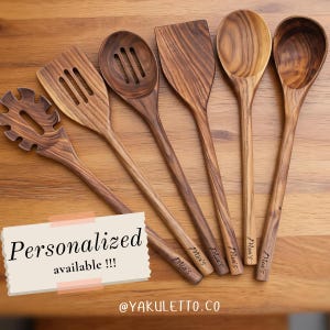 May include: A selection of wooden kitchen utensils, including a slotted spoon, spatula, and various spoons, displayed on a wooden surface. The utensils are engraved with "Mia's" and the text "Personalized available !!!" is visible. The utensils are made of light brown wood.
