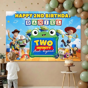 Peut inclure: Une toile de fond d'anniversaire rectangulaire avec des personnages de Toy Story dont Woody, Buzz l'Éclair et Jessie. Le texte indique HAPPY 2ND BIRTHDAY, DANIEL, et TWO INFINITY And beyond. Un cadre en forme de grenouille verte est au centre.
