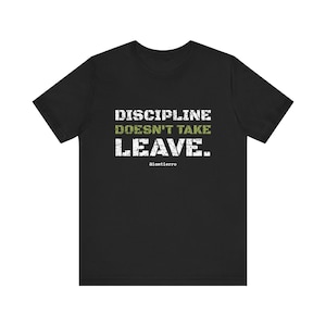 Può includere: Una t-shirt nera a maniche corte con il testo bianco dall'aspetto usurato DISCIPLINE e LEAVE, e la parola DOESN'T TAKE in verde oliva. Il piccolo testo bianco @iamtierra è stampato sotto la grafica principale sul davanti.