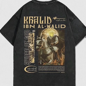 May include: Dark gray t-shirt featuring a graphic of a man on horseback with the text "KHALID IBN AL-WALID" and "SWORD OF GOD". The design includes Arabic text and a vintage aesthetic.