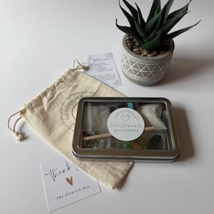 May include: A Zen garden kit in a metal tin with a clear lid, a small canvas bag, and a thank you card. The kit includes sand, stones, and a small rake. A potted succulent plant is also in the image.