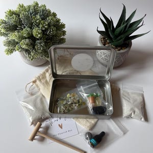 May include: A metal box containing a miniature zen garden kit, with a wooden rake, small bags of sand, and miniature vegetables. The box is surrounded by potted plants and a card that says "Thank you".