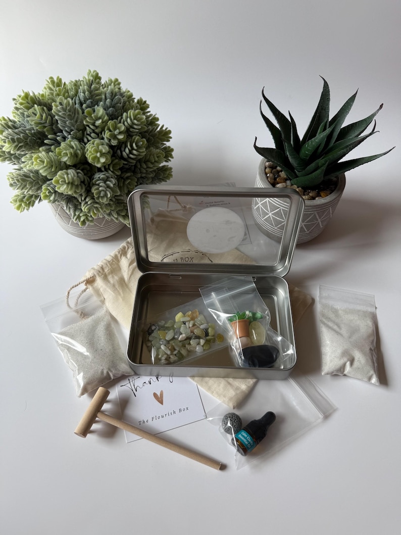 May include: A metal box containing a miniature zen garden kit, with a wooden rake, small bags of sand, and miniature vegetables. The box is surrounded by potted plants and a card that says "Thank you".