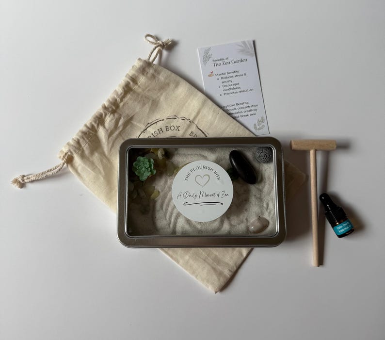 May include: A Zen garden kit featuring a metal tray, sand, decorative stones, a small wooden rake, a drawstring bag, and a bottle of essential oil. The kit includes a card detailing the benefits of a Zen garden.