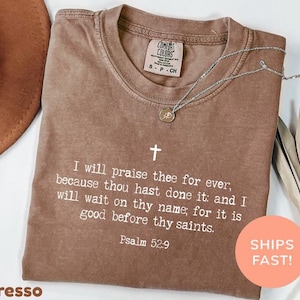 May include: A brown short-sleeved t-shirt with a white cross and the text: I will praise thee for ever, because thou hast done it: and I will wait on thy name; for it is good before thy saints. Psalm 52:9. The shirt has a Comfort Colors label.