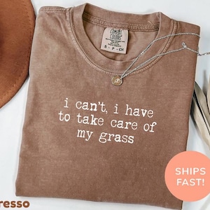 Może przedstawiać: Brązowy t-shirt z krótkim rękawem, okrągłym dekoltem i białym nadrukiem "i can't, i have to take care of my grass" z przodu. Koszulka posiada metkę marki Comfort Colors przy wewnętrznej stronie kołnierza z oznaczeniem rozmiaru S-P-CH.