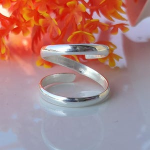 Può includere: Un anello per il piede color argento con un design a spirale. L'anello si avvolge attorno al dito del piede, creando un look unico ed elegante. L'anello è posto su uno sfondo di fiori arancioni e gialli.