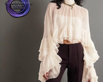 May include: A cream-colored, sheer blouse with ruffled sleeves and a high neckline. The blouse is paired with dark brown pants. The image includes a logo that says "GLAMOURGROVE BYBEA UNISEX FASHION".
