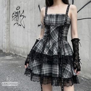 May include: A grey and black plaid dress featuring a square neckline, thin shoulder straps with metal eyelets, and a lace-up corset-style bodice. The skirt has tiered layers trimmed with black lace, and the outfit includes matching black lace gloves.