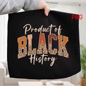 May include: Black fabric with the text "Product of BLACK History" in a mix of orange, brown, and tan colors. The word "BLACK" has a leopard print pattern. The fabric is held up by a person.