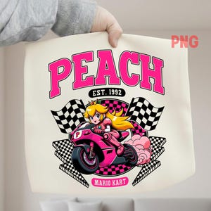 Puede incluir: Bolso tote color crema con un gráfico rosa de la Princesa Peach montada en una motocicleta rosa, con banderas a cuadros. La palabra "PEACH" está en letras rosas grandes encima de la imagen, con "EST. 1992" debajo. Las palabras "MARIO KART" están en la parte inferior.