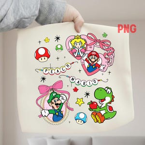 Puede incluir: Bolso tote crema con personajes de dibujos animados coloridos. El diseño incluye a Mario, Peach, Luigi y Yoshi, junto con champiñones, estrellas y el texto "PEACH MARIO". Un lazo rosa y un corazón enmarcan algunos personajes.
