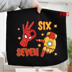 Könnte beinhalten: Schwarzer Stoff mit einer Spiderman-Hand, die das OK-Zeichen macht, und einer Iron Man-Hand, die nach unten zeigt. Die Wörter "SIX" und "SEVEN" sind in Orange gehalten, mit gelben Sternen. Ein lustiges Design für einen Geburtstag.