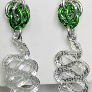 May include: Silver snake earrings with green and silver chainmaille accents. The earrings feature a detailed snake design and are suspended from silver ear wires. The chainmaille is a bright green color.