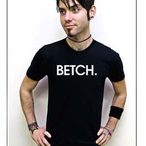 May include: Black crew neck t-shirt with the word "BETCH" in white block letters. The person is wearing a black wristband and a black choker. The person has tattoos on their arms.