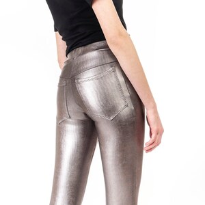May include: A woman wearing a black short-sleeve shirt and silver metallic leggings. The leggings have a shiny, textured appearance and are form-fitting. She is also wearing black high heels.
