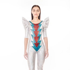 May include: A silver jumpsuit with a red and blue lightning bolt design. The jumpsuit has puffed sleeves and a scoop neck.
