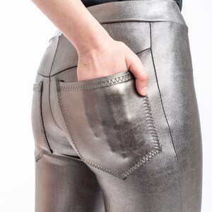 May include: Metallic silver leggings with a high waist and back pockets. The leggings have a shiny, reflective finish and are made of a stretchy material. The back pockets are outlined with a contrasting stitch.