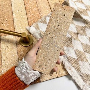 Peut inclure: Ensemble de trois mugs en céramique avec une finition mate et mouchetée. Les mugs sont de couleur crème, gris clair et gris foncé. Chaque mug a un design simple et minimaliste.