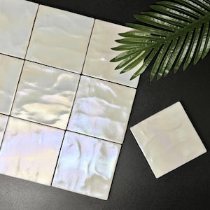 May include: A collection of square tiles with a glossy, iridescent white finish and a wavy, textured surface. The tiles are arranged in a grid pattern, reflecting light with subtle rainbow hues, accompanied by a single detached matching tile.