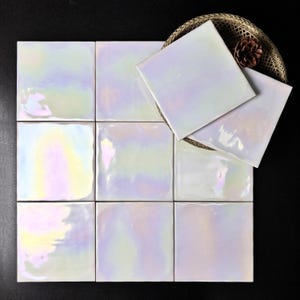 Puede incluir: Nueve baldosas cuadradas iridiscentes con acabado nacarado, dispuestas sobre una superficie oscura. Las baldosas reflejan un espectro de colores, incluyendo rosa, amarillo y azul. Una cesta tejida contiene baldosas adicionales y una piña.