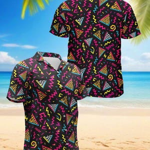 May include: Black short-sleeved shirt with a vibrant 80s-inspired geometric pattern. The design features neon pink, yellow, and blue zigzags, triangles, and checkered shapes. The shirt has a classic button-down collar.