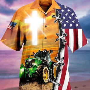 Puede incluir: Camisa de manga corta con un diseño vibrante. La camisa presenta una gran cruz blanca, un tractor verde y la bandera estadounidense. El fondo representa una puesta de sol sobre un campo y una playa.