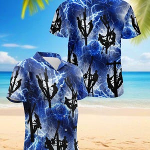 Op de afbeelding: Twee shirts met korte mouwen en knopen met een blauwe achtergrond en een bliksemflitspatroon. De shirts hebben een herhalend patroon van zwarte silhouetten van nutsarbeiders op elektriciteitspalen. De achtergrond is een blauwe lucht met witte wolken en een strandscène.